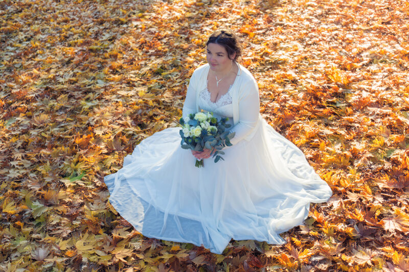 Braut in weißem Brautkleid kniet im goldenfarbenen Herbstlaub - Hochzeitsfotografie André Wolfs Mönchengladbach & NRW
